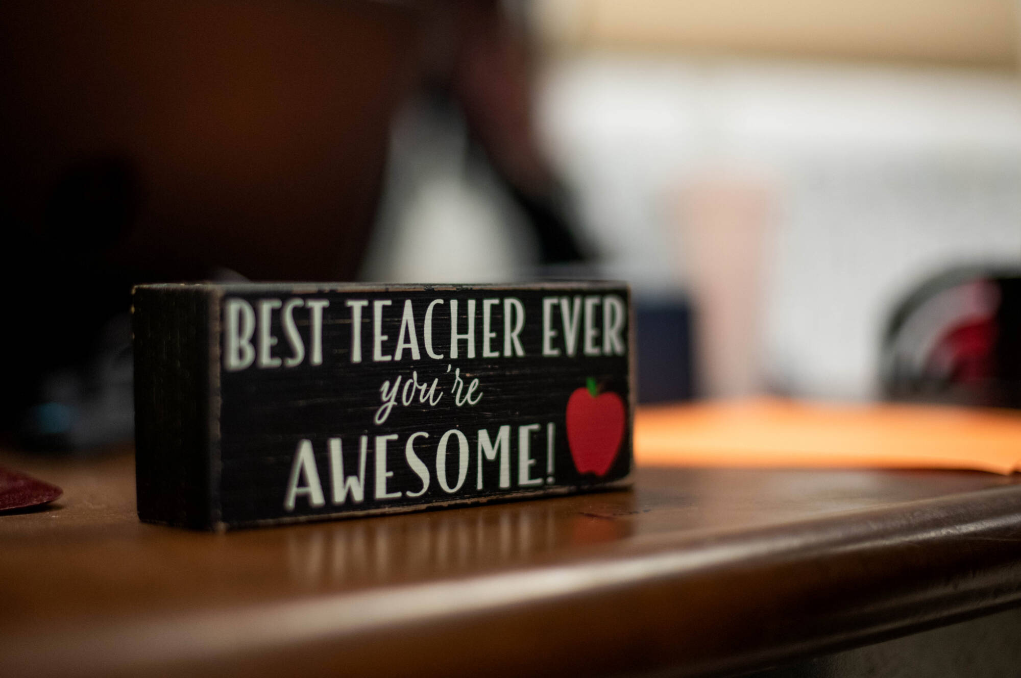 A decorative sign on a teacher's desk that says "Best Teacher Ever - You're Awesome!" with an apple graphic